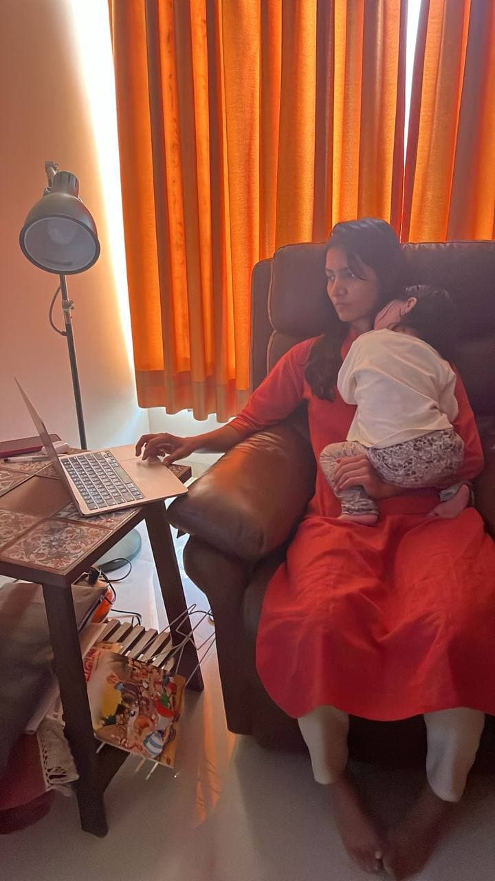 Mrugakshee working on a laptop while holding her child.